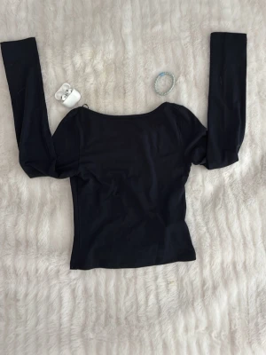 Svart långärmad topp med rund hals - En enkel och stilren svart långärmad topp med rundad halsringning. Toppen har en tight passform och är tillverkad i ett mjukt bomullsliknande material. Perfekt att matcha med jeans eller kjol för en clean look.