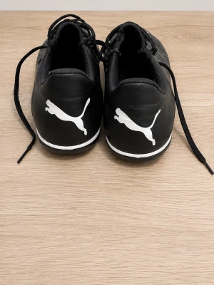 Svarta Puma fotbollsskor med snörning - Säljer ett par svarta fotbollsskor från Puma med vita detaljer och klassisk logga på häl och plös. Skorna har snörning och ovandel i syntetmaterial med små vita prickar för extra grepp. Perfekta för dig som vill ha stilrena och funktionella skor på planen. De är inte sönder och funkar exakt som ny