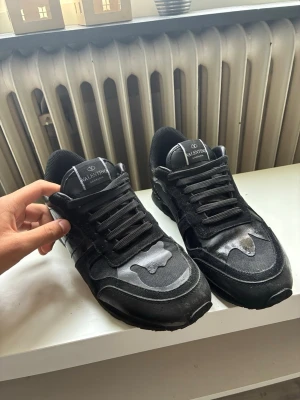 Svarta rockrunners från valentino - Snygga svarta sneakers från Valentino med coola detaljer i både mocka och läder. Skorna har svarta snören, meshpartier och en unik design på sulan. Perfekta för dig som vill ha en stilren men ändå edgy look. Passar 43 också