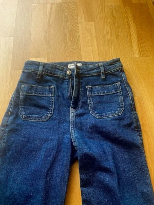 Mörkblå jeans - Snygga mörkblå jeans med raka ben och höga fickor framtill. Klassisk femficksmodell med bälteshällor och knappgylf. Jeansen har en tidlös look och är tillverkade i denim med synliga sömmar.