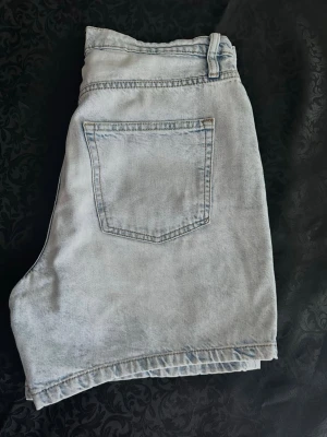 Ljusblå denimshorts med hög midja M , bomull  - Säljer ett par ljusblå denimshorts med klassisk femficksdesign och bälteshällor. Shortsen har hög midja och raka ben för en avslappnad look. Perfekta till sommaren och lätta att matcha med olika stilar.