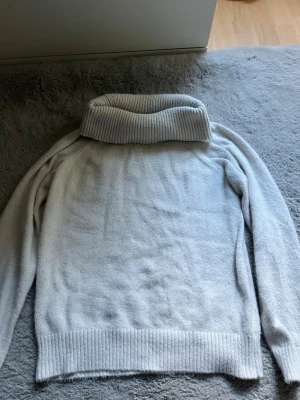 Vit polotröja från Lindex - Mysig vit stickad polotröja från Lindex med bred ribbad polokrage, ribbade muddar och nederkant. Perfekt för kalla dagar och enkel att matcha med jeans eller kjol. Tillverkad i mjukt material för extra komfort.