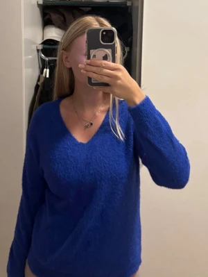 Kornblå fluffig stickad tröja - Säljer en kornblå stickad tröja med V-ringning och lång ärm. Tröjan har en mjuk, fluffig textur och avslappnad passform. Perfekt för dig som vill ha en färgklick i garderoben och gillar mysiga plagg.