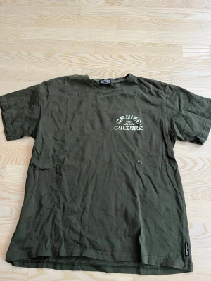 Olivgrön t-shirt med tryck - Olivgrön t-shirt med texten 'Cruise Sri Lanka Culture' tryckt i vitt på både bröstet och ryggen. Klassisk passform med rund hals och korta ärmar. Perfekt för en avslappnad och cool stil. Köpt i Sri lanka 