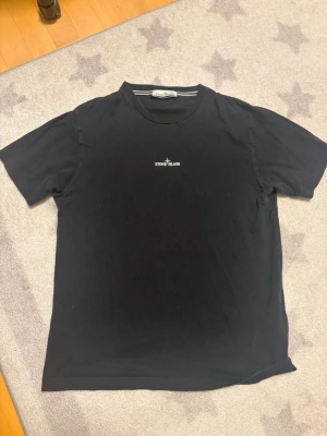 Svart t-shirt från Stone Island - Snygg svart t-shirt från Stone Island med klassisk logga broderad i vitt på bröstet. Även en logga på ryggen.
