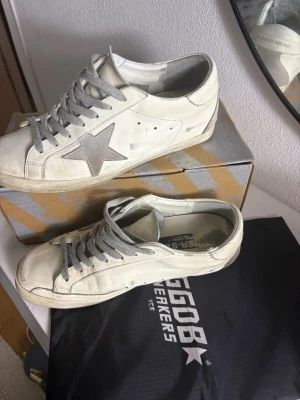 Vita sneakers med grå stjärna - Snygga vita sneakers med grå stjärndetalj på sidan och grå skosnören. Klassisk låg modell med rund tå och perforerade detaljer. Skorna har en cool streetstil och passar perfekt till jeans eller shorts. Liten skavank på 3dje bilden!