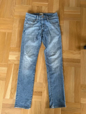 Ljusblå raka jeans med kontrastsömmar - Säljer ett par ljusblå jeans med något slimmade  ben och klassisk femficksmodell. Jeansen har slitningar framtill och bakfickor med dekorativa sömmar. Materialet är denim i bomull och passformen är normal. Perfekta för en avslappnad och trendig look.