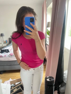 Rosa t-shirt med kort ärm - Säljer en rosa t-shirt med kort ärm och rund hals. Toppen har en tight passform och en liten broderad logga på bröstet. Perfekt för dig som gillar färg och enkel stil.