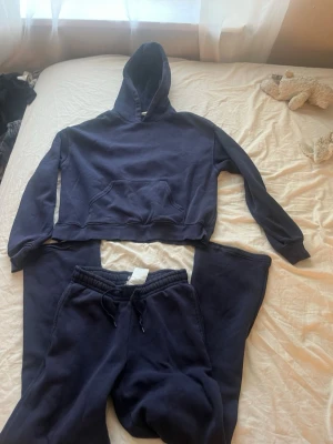 Mörkblått loungewear set med hoodie - Mysigt mörkblått loungewear set med hoodie och matchande byxor. Hoodien har magficka och dragsko i huvan, byxorna har resårmidja och dragsko för skön passform. Perfekt för chill dagar hemma eller när du vill vara bekväm.