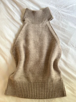 Beige stickad ärmlös polotröja Zara - Stickad topp från Zara. Tröjan har hög ribbad polokrage och bred ribbad kant nedtill. Perfekt till höst och vinter. Aldrig använd
