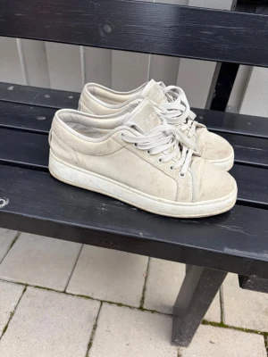 Beige låga sneakers från ETQ - Snygga beige sneakers från ETQ i mocka med klassisk låg profil och vita snören. Skorna har en stilren design med ton-i-ton detaljer och en vit sula. Perfekta för dig som gillar minimalistisk och clean stil.