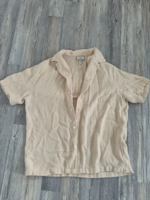 Beige kortärmad skjorta från H&M - Säljer en beige kortärmad skjorta från H&M i regular fit. Skjortan har en strukturerad yta, klassisk krage och knappar framtill. Perfekt för dig som gillar en enkel men ändå stilren look.