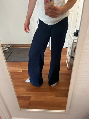 Mörkblå utsvängda jeans - Säljer ett par mörkblå jeans med utsvängda ben och vita kontrastsömmar. Jeansen har klassisk femficksmodell och hög midja. Perfekta för dig som gillar en retroinspirerad look och vill ha ett par bekväma och stilrena jeans. Aldrig använda💙🩵