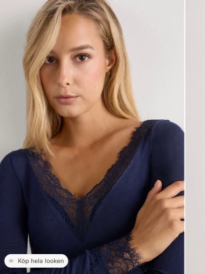Intimissimi topp - Snygg mörkblå långärmad topp med v-ringning och spetsdetaljer längs halsringningen och ärmsluten. Toppen har en slim passform och är tillverkad i ett mjukt material som sitter skönt på kroppen. Perfekt för dig som vill ha en stilren men ändå feminin look.