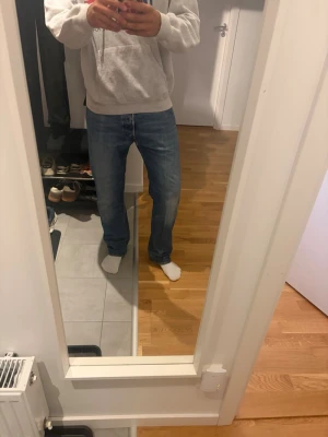 Levi's 501 blå raka jeans - Klassiska blå Levi's 501 jeans med rak passform och normal midja. Jeansen har fem fickor, knappgylf och den ikoniska läderlappen bak i midjan. Tillverkade i slitstark denim med snygg tvätt och röda Levi's-taggen på bakfickan. Hål mellan benen på sista bilden, därav priset!