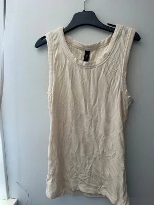 Ribbad beige linnetopp från Y.A.S - Säljer en ribbad beige linnetopp från Y.A.S. Toppen är ärmlös med breda axelband och har en rund halsringning. Perfekt att styla till jeans eller kjol för en enkel och fräsch look.