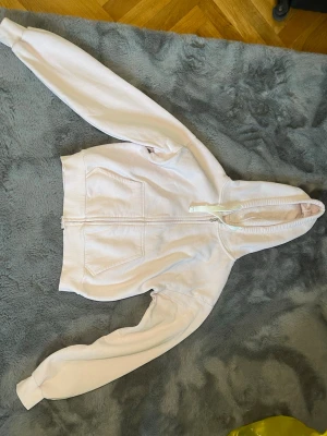 Ljusrosa hoodie med dragkedja - Säljer en ljusrosa hoodie med dragkedja och två stora fickor framtill. Hoodien har huva med snören och ribbade muddar vid ärmslut och midja. Perfekt för en chill och avslappnad stil. Materialet känns mjukt och bekvämt. Finns en fläck har inte riktigt försökt tvätta bort den men den borde nog försvinna i en tvätt med galltvål.