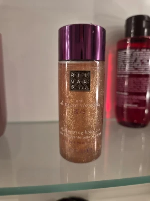 Shimmering body oil Rituals - Shimmering body oil från Rituals, The Ritual of Yozakura. Oljan har en skimrande guldig färg och kommer i en genomskinlig plastflaska med lila lock. 