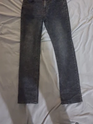 Grå tvättade raka jeans - Säljer ett par grå tvättade jeans med rak passform och klassisk femficksdesign. Jeansen har en snygg vintagekänsla och är tillverkade i ett robust denimtyg. Perfekta för dig som gillar en avslappnad men ändå stilren look.