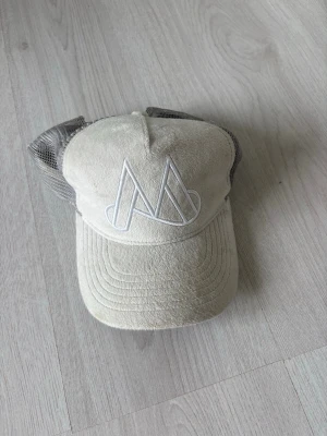 Beige keps från Maggiore - Snygg beige keps från Maggiore med vit broderad logga framtill. Kepsen har mesh på sidorna och bak för extra ventilation och justerbar rem baktill. Perfekt accessoar för en avslappnad och trendig stil.