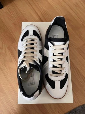 Svarta och vita sneakers med gummisula - Snygga sneakers i svart och vitt med klassisk design och beige snörning. Skorna har en låg profil och en slitstark gummisula som ger bra grepp. Ovandelen är i tyg och detaljerna i svart skapar en cool kontrast mot det vita.