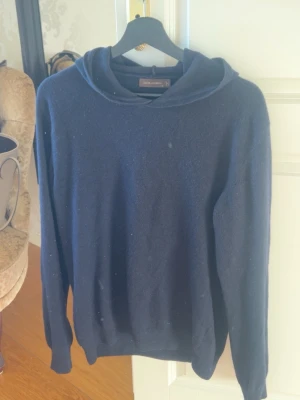 Mörkblå hoodie i mjukt material - En enkel och stilren mörkblå hoodie med huva. Tillverkad i ett mjukt, stickat material som känns skönt mot huden. Hoodien har långa ärmar och en avslappnad passform, perfekt för en chill och casual look.
