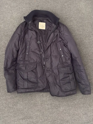 Moncler Jacka - Snygg mörkblå dunjacka från Moncler med hög krage, dragkedja och knappar framtill. Jackan har stora fickor med lock och knappstängning samt ribbade detaljer vid kragen. Perfekt för kalla vinterdagar och riktigt stilren look. Storlek 2~ S/M. Skick 8,5/10, vänsterficka där fram har tappat knapp men märks ej vid använding! Fler frågor eller funderingar hör av er i Dm🙌