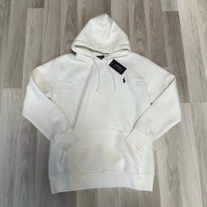 Vit hoodie  - Snygg vit hoodie med klassisk huva och dragsko. Har en liten broderad logga på bröstet och en stor magficka framtill. Tillverkad i mjukt material som passar perfekt för kyliga dagar. Väldigt tjockt material, perfekt för vintern/hösten! Står storlek XXL men är storlek S.