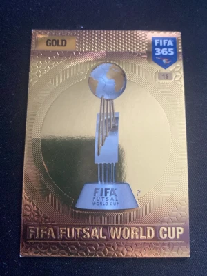 FIFA Futsal World Cup guld-kort - Säljer ett exklusivt samlarkort i guld från FIFA 365-serien med motiv av FIFA Futsal World Cup-trofén. Kortet har en glänsande guldfärgad yta och detaljerad design, perfekt för dig som gillar fotboll och samlarobjekt.