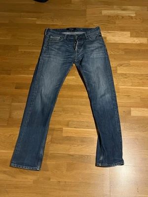 Blå raka jeans från Replay - Snygga blå jeans från Replay med klassisk femficksmodell och raka ben. Jeansen har en tvättad look med subtila slitningar och är tillverkade i ett mjukt denimtyg. Perfekta för en avslappnad och trendig stil.