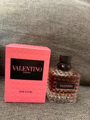 Valentino Donna Born In Roma parfym - Valentino Donna Born In Roma är en lyxig parfym i en elegant, rosa-färgad glasflaska med nitar och svart lock. Förpackningen är rosa med svart etikett och text i rosa. Flaskan har en exklusiv design som känns både modern och klassisk.