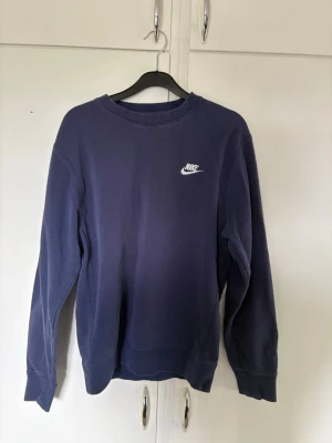 Mörkblå tröja från Nike - En stilren mörkblå sweatshirt från Nike med klassisk logga på bröstet. Tröjan har rund halsringning och långa ärmar. Perfekt för en avslappnad och sportig look. Bra skick