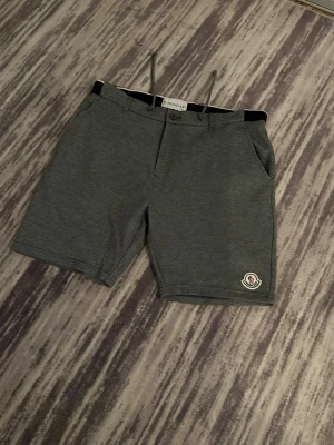 Moncler shorts i grått och vitt svart  - Moncler shorts, ett par i mörkgrått ,vitt och svart  alla  har snörning i midjan, sidofickor och Moncler-logga på benet. Klassisk design med bekväm passform och diskreta detaljer. Perfekta för sommaren.