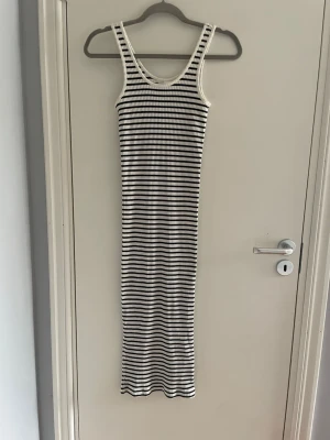 Randig långklänning i ribbad bomull - Säljer en lång, ärmlös klänning med svarta och vita ränder. Klänningen är ribbad och har en kroppsnära passform med rundad halsringning. Perfekt för varma dagar och enkel att styla med sneakers eller sandaler.