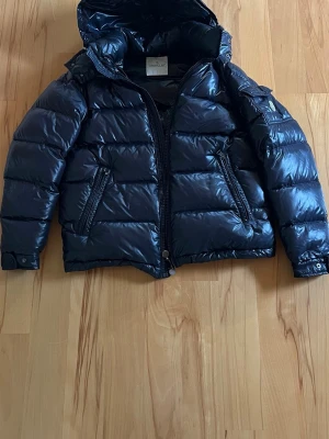 Svart dunjacka från Moncler - Snygg svart dunjacka från Moncler med glansig finish och huva. Saknar cartoon lapp, men annars fint skick. Köpt från merchsweeden!☺️