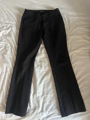 Svarta kostymbyxor med bootcut - Snygga svarta kostymbyxor med bootcut och pressveck. Byxorna har fickor fram och bak samt hällor för skärp. Klassisk och stilren modell i ett slätt tyg som passar till många olika looks. Dom är storlek 38 men skulle säga att dom passar som 36