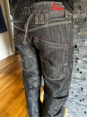 Replay svarta jeans med kontrastsömmar - Säljer ett par svarta jeans från Replay med vita kontrastsömmar och röda detaljer. Jeansen har stora bakfickor med unik söm, bälteshällor och Replay-logga broderad i rött bak. Snygg streetstil och avslappnad passform. Midja 45 cm Ben innermått 86 cm . 