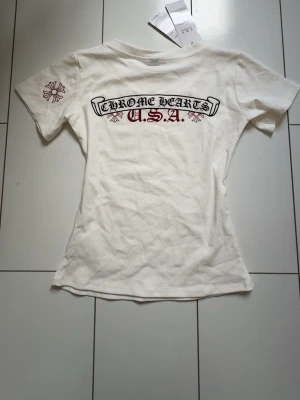 Vit V ringad t-shirt med Chrome hearts tryck - Jag säljer en jätte fin figur sydd t-shirt med Chrome hearts tryck!❤️ Den är aldrig använd! T-shirten är tillverkad i mjuk bomull så den är inte genomskinlig alls! Trycket är inte heller glansigt  och den passar till allt!❤️ skriv om ni har mer frågor! Är öppen för prisförslag !