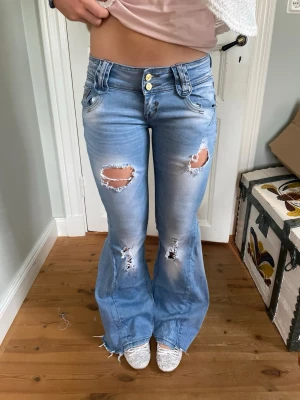 Lågmidjade bootcut jeans med slitningar - Säljer dessa lågmidjade jeans som är omsydda till bootcut. Midjemått 36 cm och innerbenslängd 78 cm. Jeansen är i stretchigt matrial. 