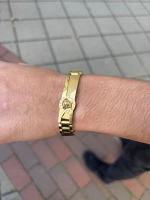 Guldigt länkarmband - Snyggt armband i guldfärgad metall med länkdesign och ett detaljerat märke på ovansidan. Armbandet har en stilren och klassisk look som passar perfekt till dig som vill sticka ut med accessoarer. Lätt att matcha med olika outfits. Längden på armbandet:19CM