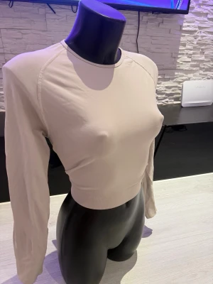 Beige långärmad crop top - Trendig beige crop top med långa ärmar och rund halsringning. Tillverkad i ett stretchigt och mjukt material som sitter tight mot kroppen. Perfekt att matcha med höga jeans eller kjol för en snygg och enkel look.