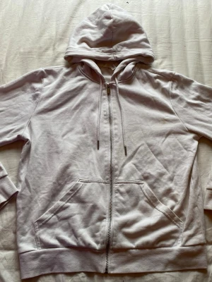 Vit zip hoodie med huva - En basic vit hoodie med dragkedja framtill och justerbar huva med snören. Hoodien har två stora fickor på magen och ribbade muddar vid ärmslut och nederkant. Har en liten fläck på framsidan som eventuellt kan gå bort med nått medel har ej testat själv 