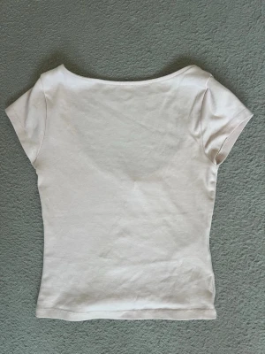 Ljusrosa kortärmad topp - En enkel och stilren ljusrosa topp med korta ärmar boatneck urringning i nacken. Toppen har en tight passform och är tillverkad i mjukt bomullsmaterial, perfekt för en clean och fräsch look.