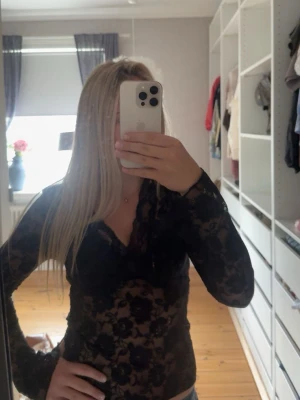 Svart spetsblus från Gina Tricot - Säljer en svart långärmad spetsblus från Gina Tricot med blommigt mönster och v-ringning. Blusen är genomskinlig och har en slim passform. (Storlek M men sitter som en S) använd ändast fåtal gånger. 