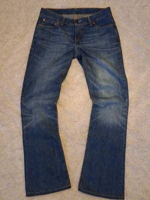 Bootcut jeans från Levi's - Klassiska blå jeans från Levi's med bootcut-passform och fem fickor. Jeansen har en snygg tvätt med lätt slitning och detaljerade sömmar. Tillverkade i denim med en autentisk känsla och ikonisk läderpatch bak i midjan.