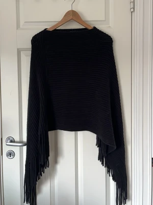 Svart ribbad poncho med fransar - Snygg svart ribbad poncho från Åhléns. Jätteskönt material