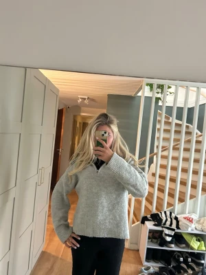 Grå stickad tröja med krage - Mysig grå stickad tröja med bred ribbad krage och dragkedja framtill. Tröjan har långa ärmar och ribbade muddar vid ärmslut och nederkant. Perfekt för kyliga dagar och enkel att styla till olika outfits.