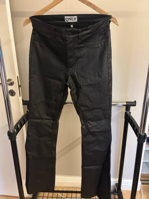 Svarta coated jeans från ONLY - skinlook byxor från Only, Låssas fickor fram men vanliga bak. Knapp och dragkedja i midjan, utsvängda med stretch. Aldrig använda 