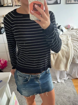 Svart tröja med vita ränder - Säljer en svart långärmad tröja med tunna vita horisontella ränder. Tröjan har rund halsringning och en avslappnad passform. Perfekt till jeans eller kjol för en enkel och stilren look.