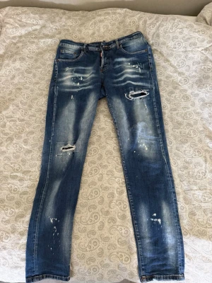 Blå slitna jeans från Dsquared2 - Säljer ett par blå jeans från Dsquared2 med slitningar. klassisk femficksdesign och är tillverkade i denim. Perfekta för en trendig och avslappnad look.